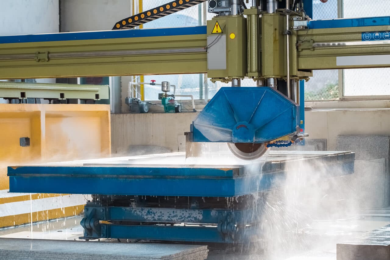Bridge saw cutting a stone slab under a spray of water